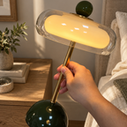 En hånd som holder en fin grønn glass lampe ved et nattbord.