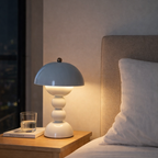 Hvit led lampe på et nattbord ved siden av en seng med hvitt sengetøy. 
