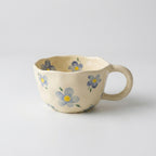 Koselig håndlaget kaffekopp i keramikk med blomster i et hvitt studio. 