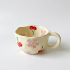 Koselig håndlaget kaffekopp i keramikk med blomster i et hvitt studio. 