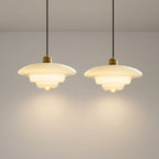 To pendell taklamper i glass i et grått rom.