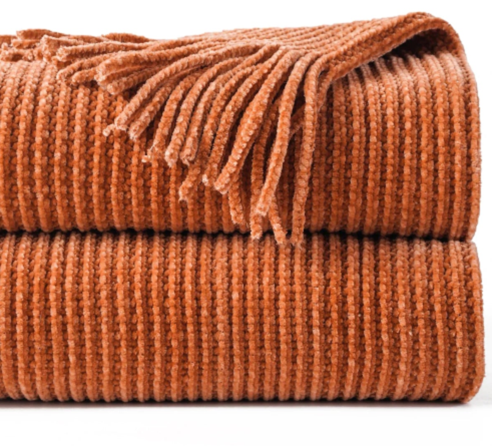 Pledd i oransje med fringe detaljer i et hvitt studio. 