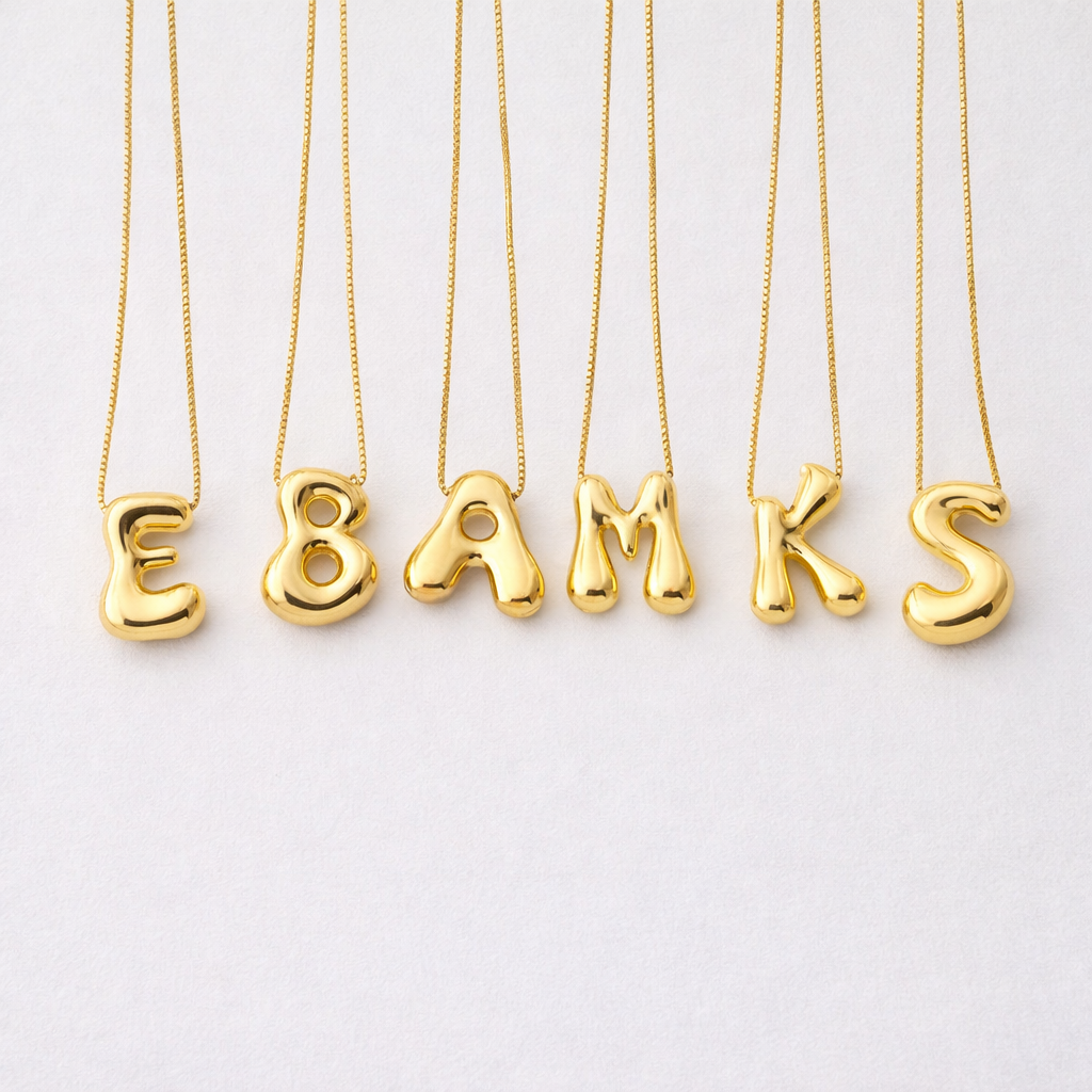 Bostavsmykker i gull i stainless steel i et studio. 