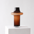 Unik formet glassvase i brunfarge i et hvitt studio.