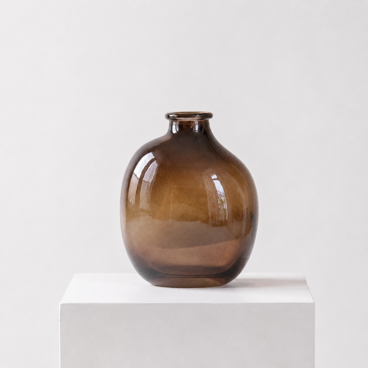 Glass vase in brown on a white stand in a white studio