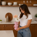 Jente som holder rosa transparent vase på et kjøkken.