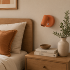 Oransje vegglamp over et nattbord i et koselig soverom. 