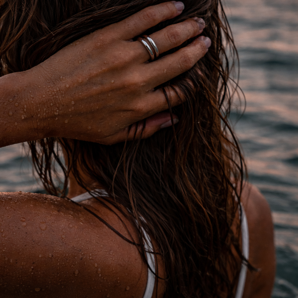 Jente i sjøen med hånden i håret og en sølv dobbelring på hånden.