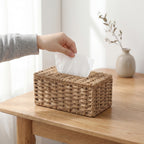 En hånd som drar opp tørkepapir fra en rattan papirholder.