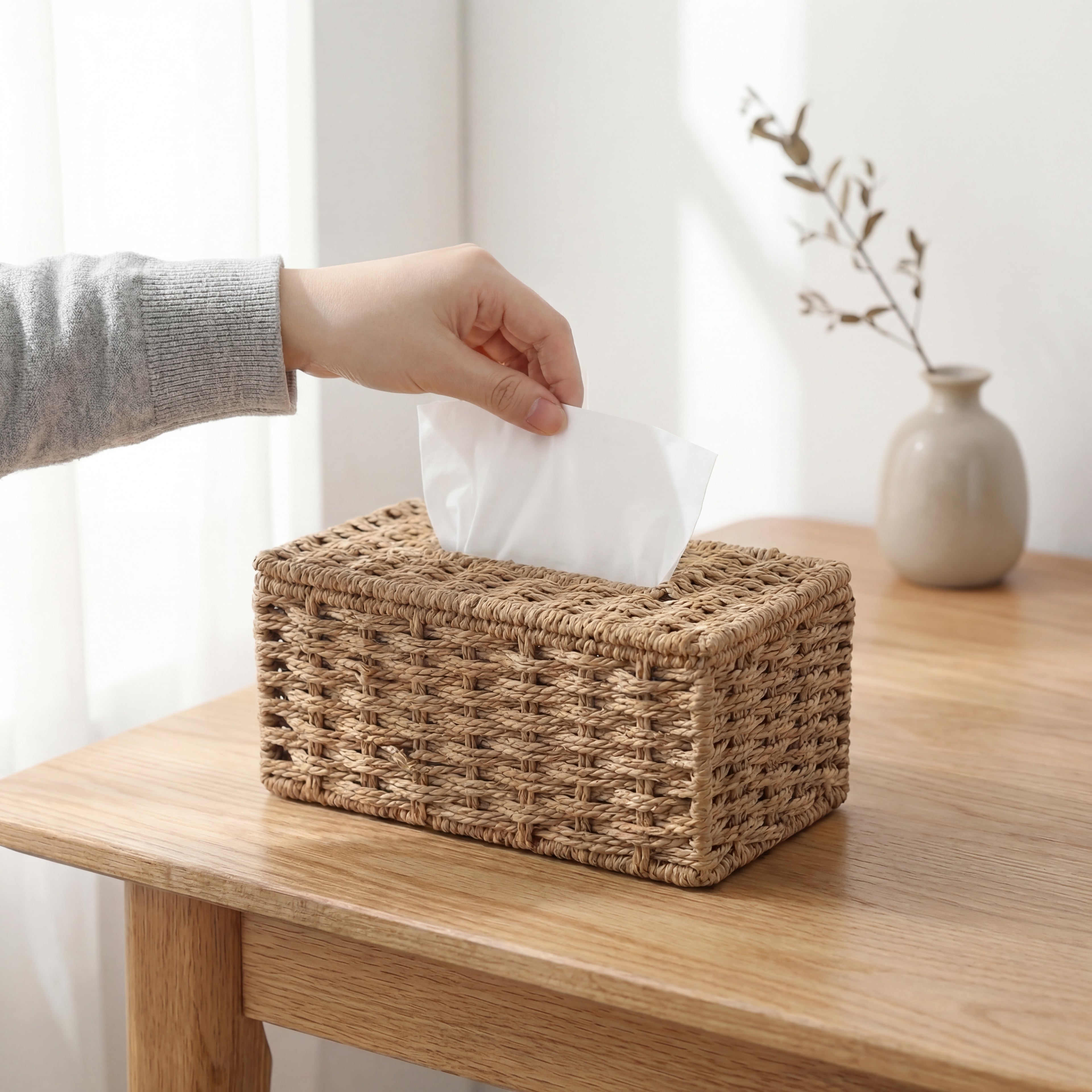 En hånd som drar opp tørkepapir fra en rattan papirholder.