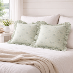 To søte grønne puter med volanger og print i en koselig seng. 