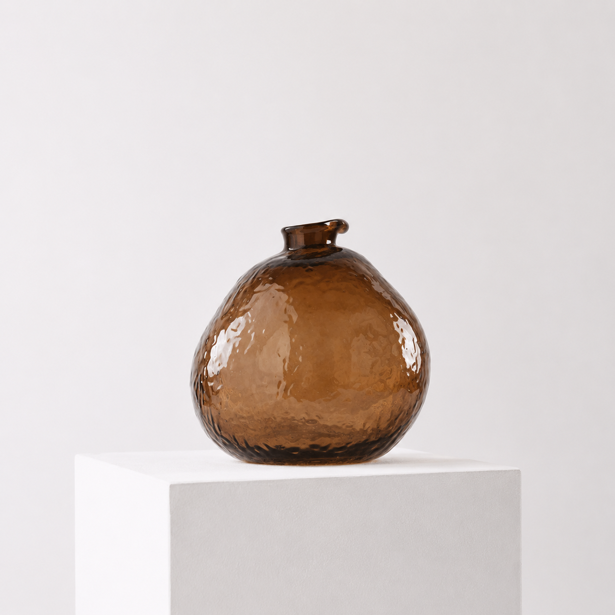 Brun rund unik vase på en hvit stand i et hvitt studio.
